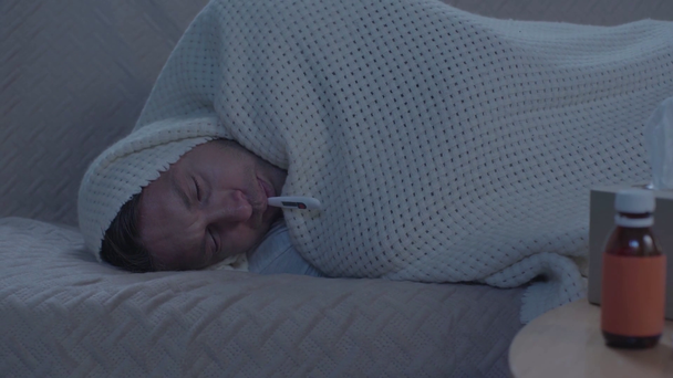 beteg ember feküdt a kanapén, csomagolás takaró és a hőmérséklet mérése - Felvétel, videó