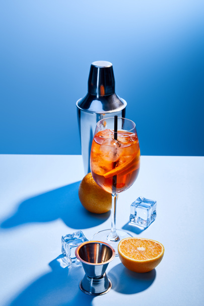 cocktail Aperol Spritz, oranges, shaker, ice cubes and measuring cup on blue background  - Photo, Image
