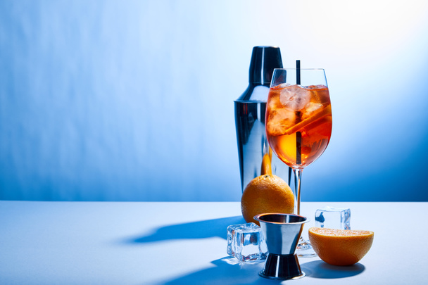 cocktail Aperol Spritz, oranges, shaker, ice cubes and measuring cup on blue background  - Fotoğraf, Görsel