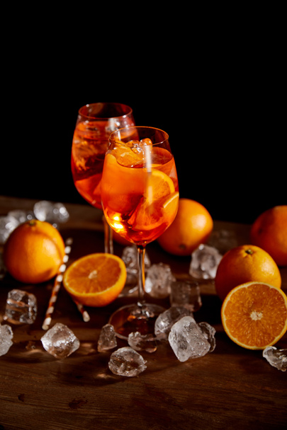 selective focus of Aperol Spritz in glasses, oranges and ice cubes on black background  - Fotó, kép