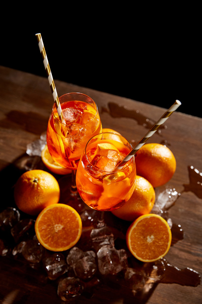 high angle view of Aperol Spritz in glasses, oranges and ice cubes on black background  - Foto, Imagem