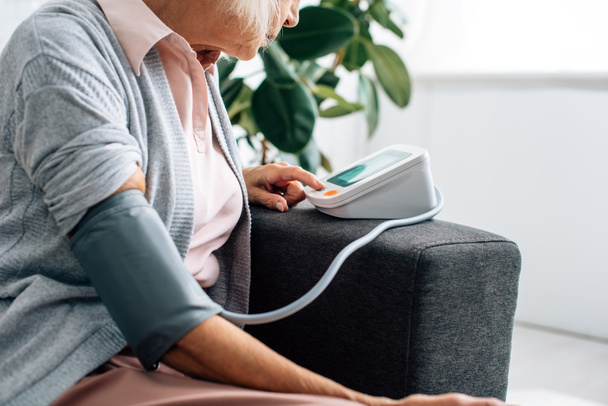 vista ritagliata di donna anziana seduta sul divano e misurazione della pressione sanguigna in appartamento
  - Foto, immagini