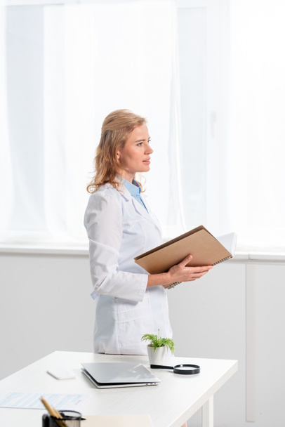 side view of attractive nutritionist holding notebook in clinic  - Photo, Image