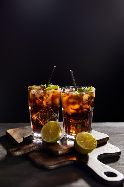 cocktails cuba libre σε ποτήρια με καλαμάκια και λάιμ σε μαύρο φόντο  - Φωτογραφία, εικόνα