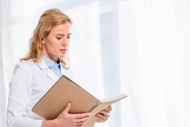 attractive nutritionist holding and reading notebook in clinic  - Zdjęcie, obraz