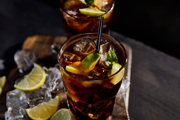 foyer sélectif de cocktails cuba libre dans des verres avec des pailles, des glaçons et des citrons verts sur fond noir
  - Photo, image