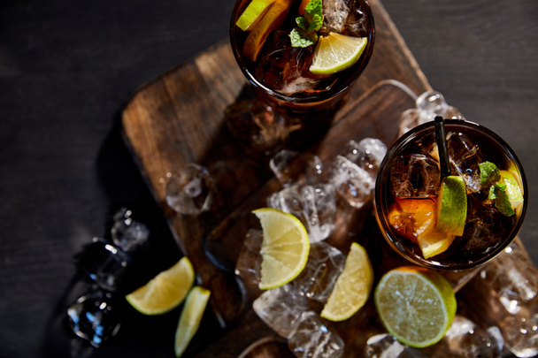 vue de dessus des cocktails cuba libre dans des verres avec des pailles, des glaçons et des citrons verts sur fond noir
  - Photo, image