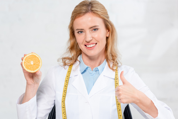 nutritionniste souriant avec ruban à mesurer tenant coupé orange et montrant comme à la clinique
  - Photo, image