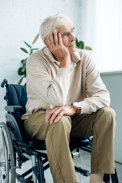 handsome and dreamy senior man sitting in wheelchair in apartment  - Foto, immagini