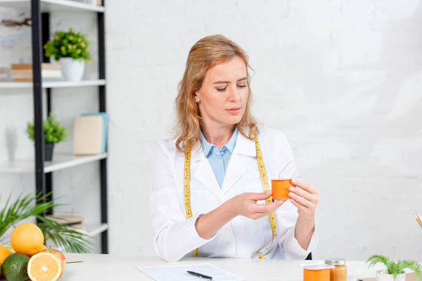 nutritionniste attrayant assis à table et tenant du yaourt à la clinique
  - Photo, image