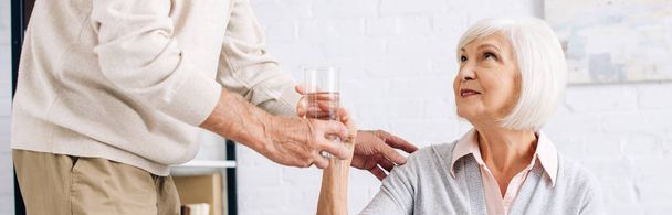panoramic shot of husband giving glass of water to wife in apartment  - Fotoğraf, Görsel