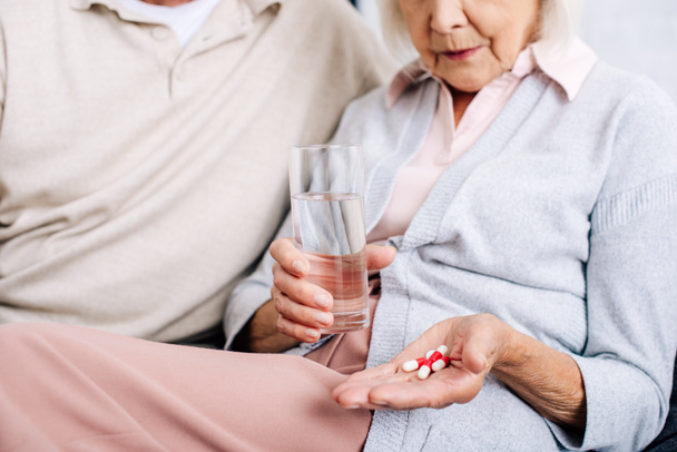 vista cortada de marido e mulher segurando vidro e pílulas no apartamento
  - Foto, Imagem