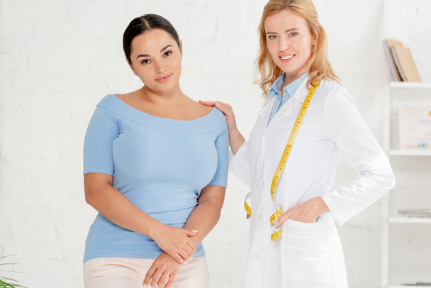 attractive nutritionist and patient looking at camera in clinic  - Photo, Image