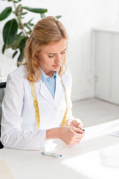 привабливий дієтолог сидить за столом і тримає глюкометр у клініці
  - Фото, зображення
