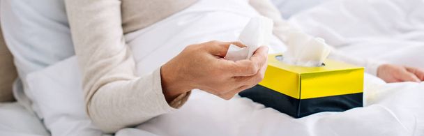 panoramic shot of ill senior woman holding napkin in bed  - Foto, afbeelding