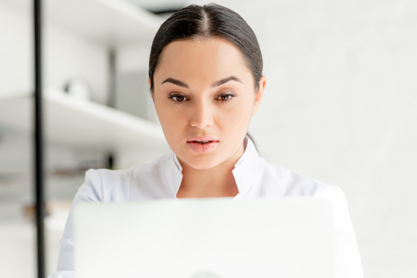 selective focus of attractive dermatologist using laptop in clinic  - Foto, imagen