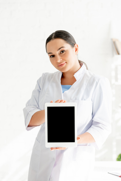 attractive dermatologist holding digital tablet and looking at camera in clinic  - Foto, imagen