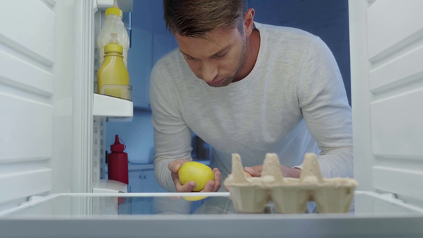 hungry man taking apple and lemon from fridge and putting them back - Footage, Video