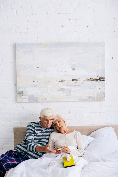 όμορφος σύζυγος και η γυναίκα κοιτάζοντας θερμόμετρο στο διαμέρισμα  - Φωτογραφία, εικόνα