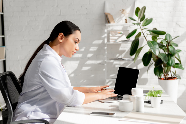 attractive dermatologist sitting at table and using laptop in clinic  - Foto, imagen