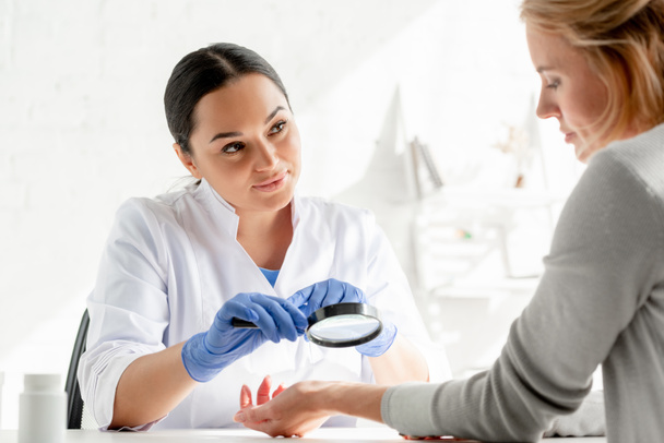 dermatolog badający skórę pacjenta ze szkłem powiększającym w klinice - Zdjęcie, obraz