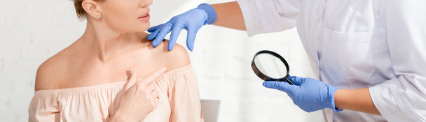 plano panorámico del dermatólogo examinando la piel del paciente con lupa en la clínica
 - Foto, Imagen