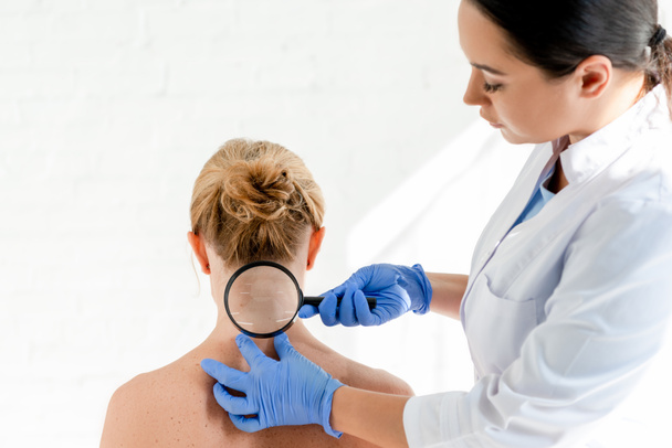 Dermatologe untersucht Haut von Patientin mit Lupe in Klinik - Foto, Bild
