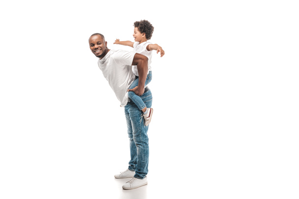cheerful african american man piggybacking adorable son and smiling at camera on white background - Fotó, kép