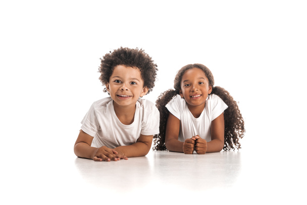 glücklich afrikanisch-amerikanische Bruder und Schwester lächeln in die Kamera, während sie auf weißem Hintergrund liegen - Foto, Bild