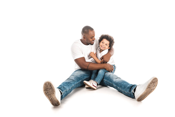 happy african american man hugging cute son while sitting on white background - Photo, Image