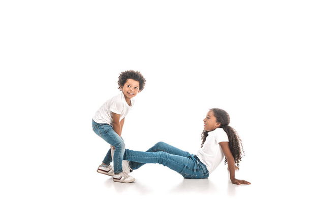 cheerful african american boy dragging sister by leg on white background - Foto, Bild