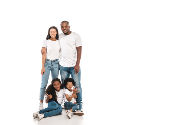 smiling african american man hugging wife while standing near chidren sitting on white background - Photo, Image