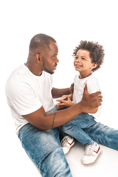 handsome african american man talking to smiling son on white background - Фото, изображение