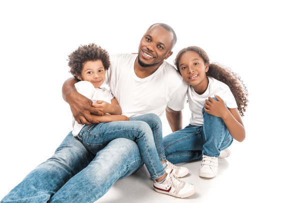 glücklich afrikanisch-amerikanischer Mann umarmt Sohn und Tochter, während er zusammen auf weißem Hintergrund sitzt - Foto, Bild