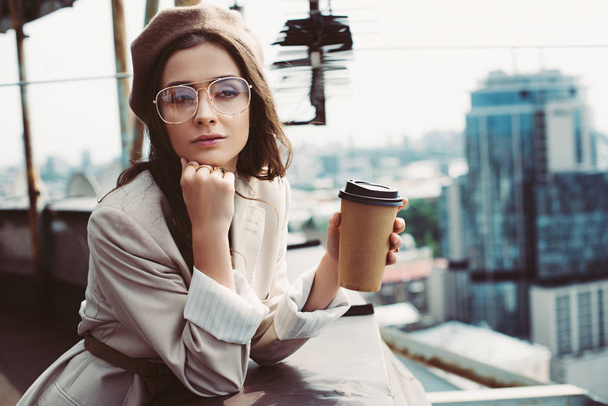 elegant pensive girl in beige suit and beret posing on roof with coffee to go - Photo, Image