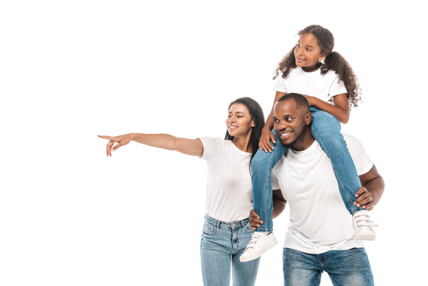 cheerful african american woman pointing with finger, and husband piggybacking adorable daughter isolated on white - Valokuva, kuva