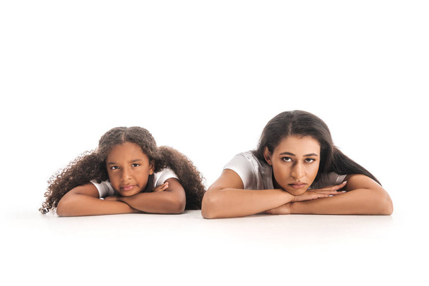 upset african american mother and daughter looking at camera while lying on white background - Photo, Image