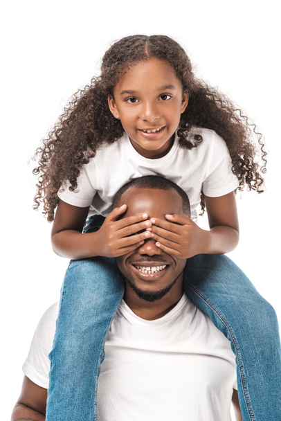 fröhliche afrikanisch-amerikanische Kind bedeckt Väter Augen mit den Händen, während huckepack isoliert auf weiß - Foto, Bild
