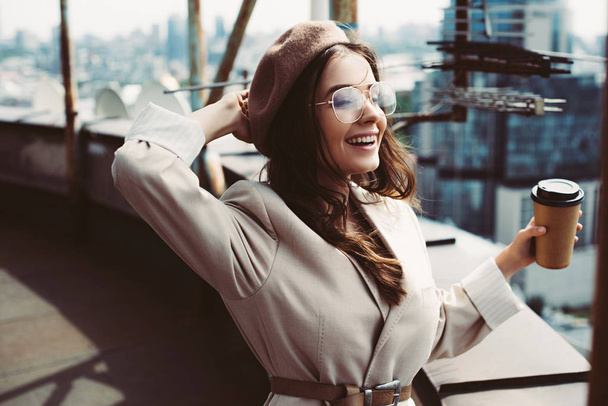 attractive happy girl in beige suit and beret posing on roof with coffee to go - Foto, Imagem
