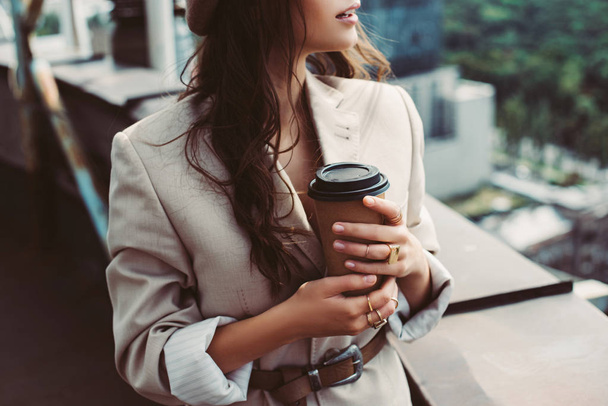 cropped view of fashionable girl in beige suit posing on roof with coffee to go - 写真・画像