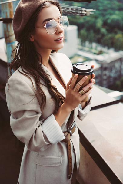 attractive fashionable girl in beige suit and beret posing on roof with coffee to go - Foto, Bild