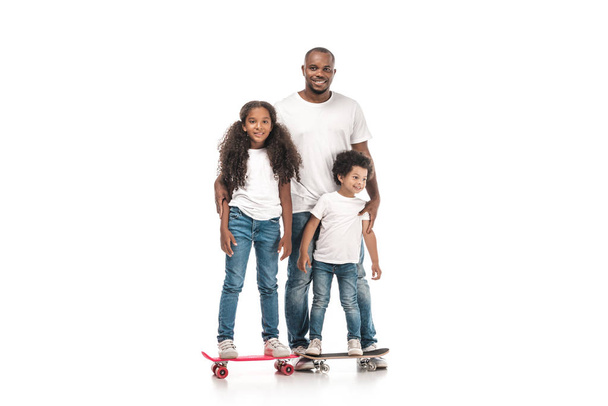 alegre afroamericano hombre cerca de hija de pie en monopatín, e hijo en penny board sobre fondo blanco
 - Foto, Imagen