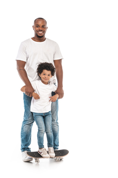 happy african american man supporting adorable son standing on penny board on white background - Foto, immagini