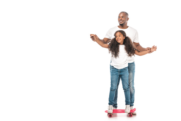 smiling african american father supporting adorable daughter skateboarding on white background - 写真・画像