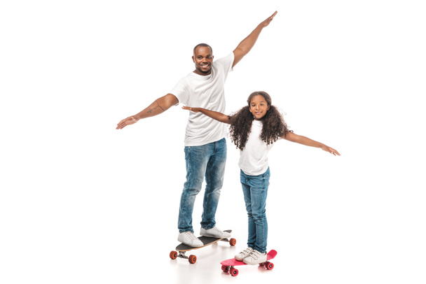 Ευτυχισμένος αφρικανός πατέρας και κόρη ισορροπώντας στο longboard και πατινάζ σε λευκό φόντο - Φωτογραφία, εικόνα