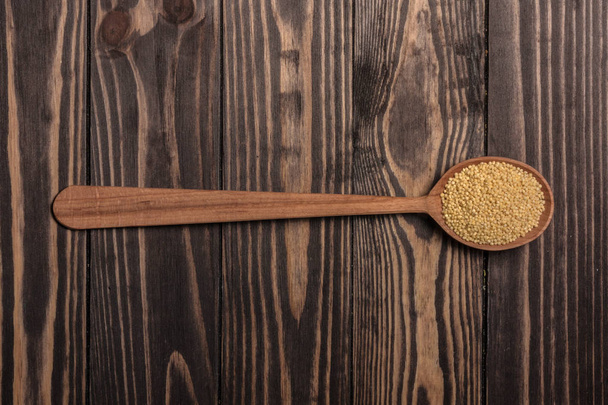 Una cuchara de madera con mijo se encuentra en tablas de madera marrón oscuro
. - Foto, imagen