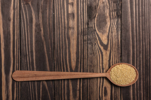 Une cuillère en bois avec millet repose sur des planches de bois brun foncé
. - Photo, image
