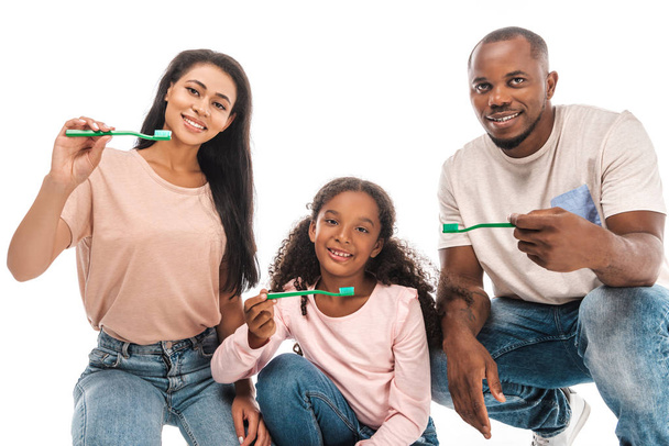 felici genitori afro-americani con figlia che tiene spazzolini da denti e sorride alla telecamera isolata su bianco
 - Foto, immagini