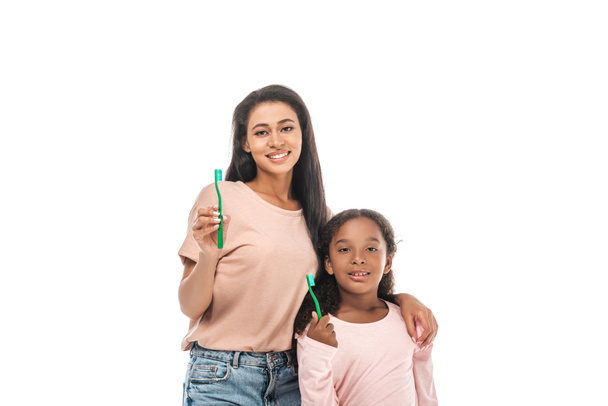 cheerful african american mother and daughter holding toothbrushes and smiling at camera isolated on white - Fotografie, Obrázek