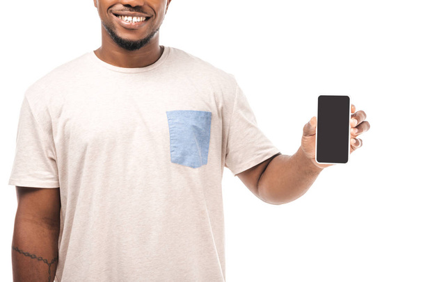 částečný pohled na usmívající se africký Američan drží smartphone s prázdnou obrazovkou izolované na bílé - Fotografie, Obrázek